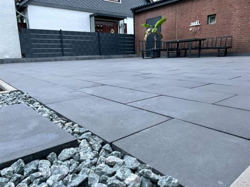 Grauer Pflasterboden mit Kies und Sitzgelegenheit in einem Innenhof.