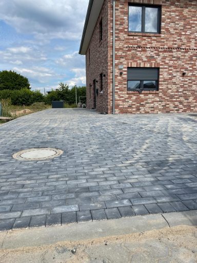 Steinerne Auffahrt vor einem Ziegelbau mit bewölktem Himmel im Hintergrund.